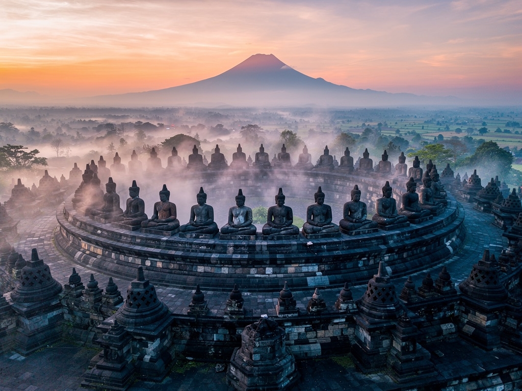 Candi Borobudur saat fajar dengan latar pegunungan dan kabut tipis, suasana spiritual yang tenang